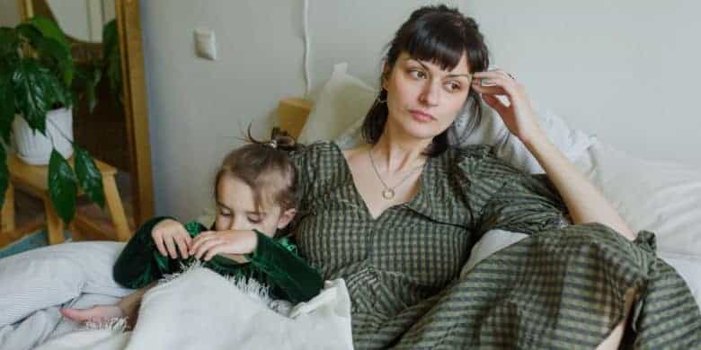 tired mother with cute daughter resting on bed in cozy room
