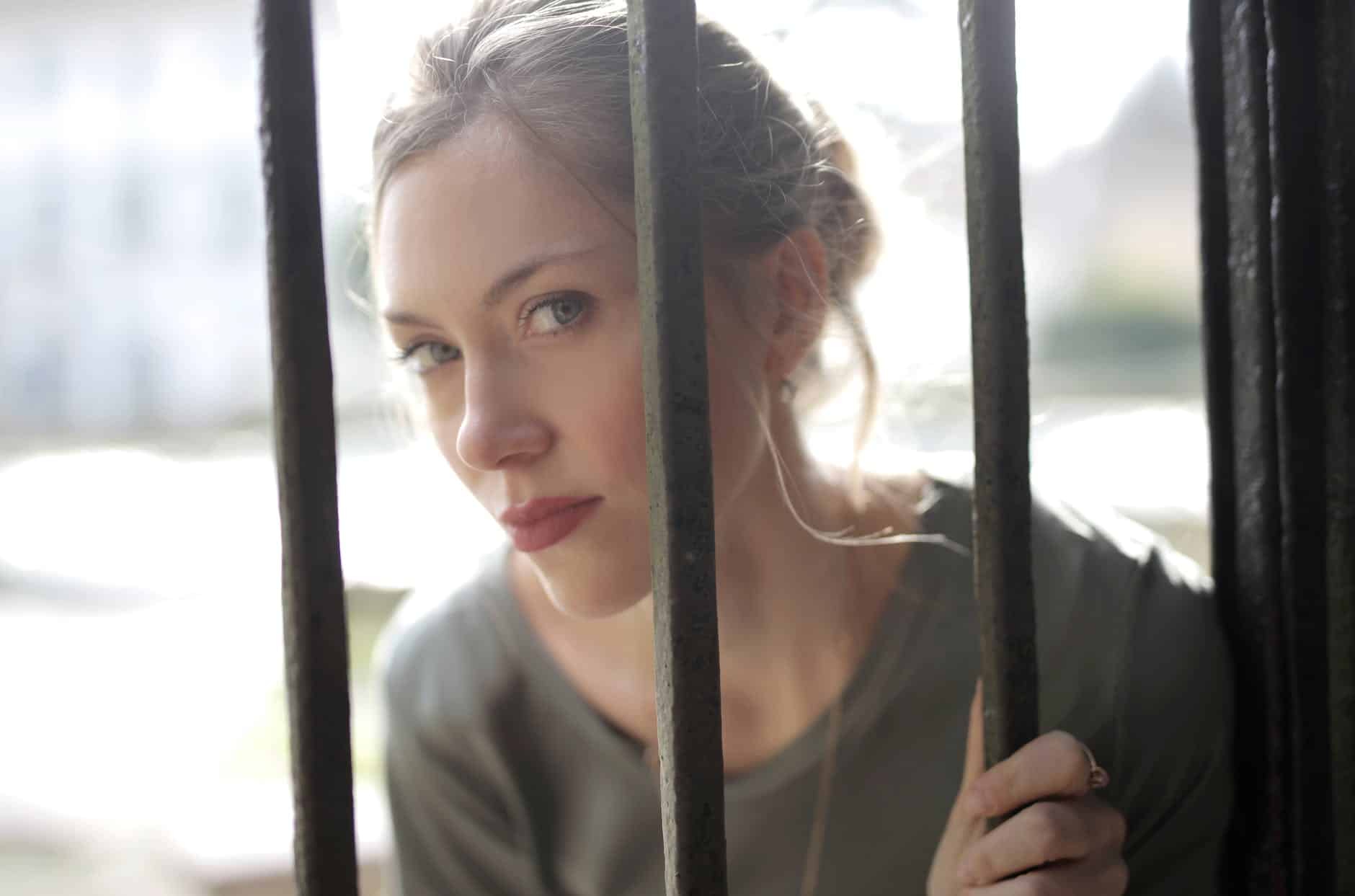 young gorgeous woman standing behind iron grate