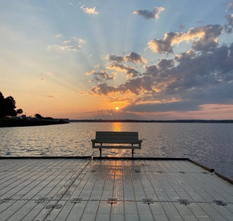 bench on a boardwalk near a body of water at sunset