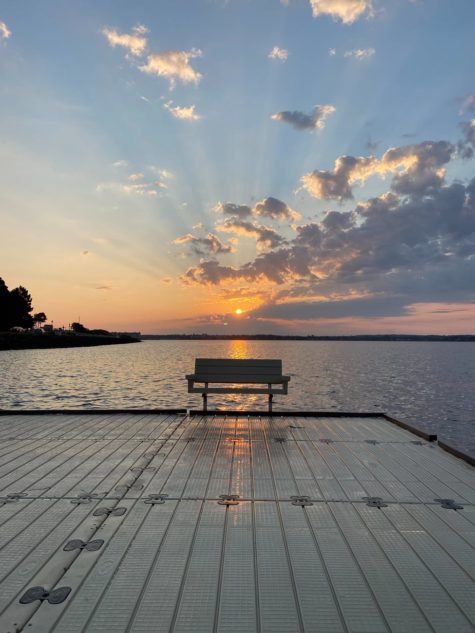 bench on a boardwalk near a body of water at sunset